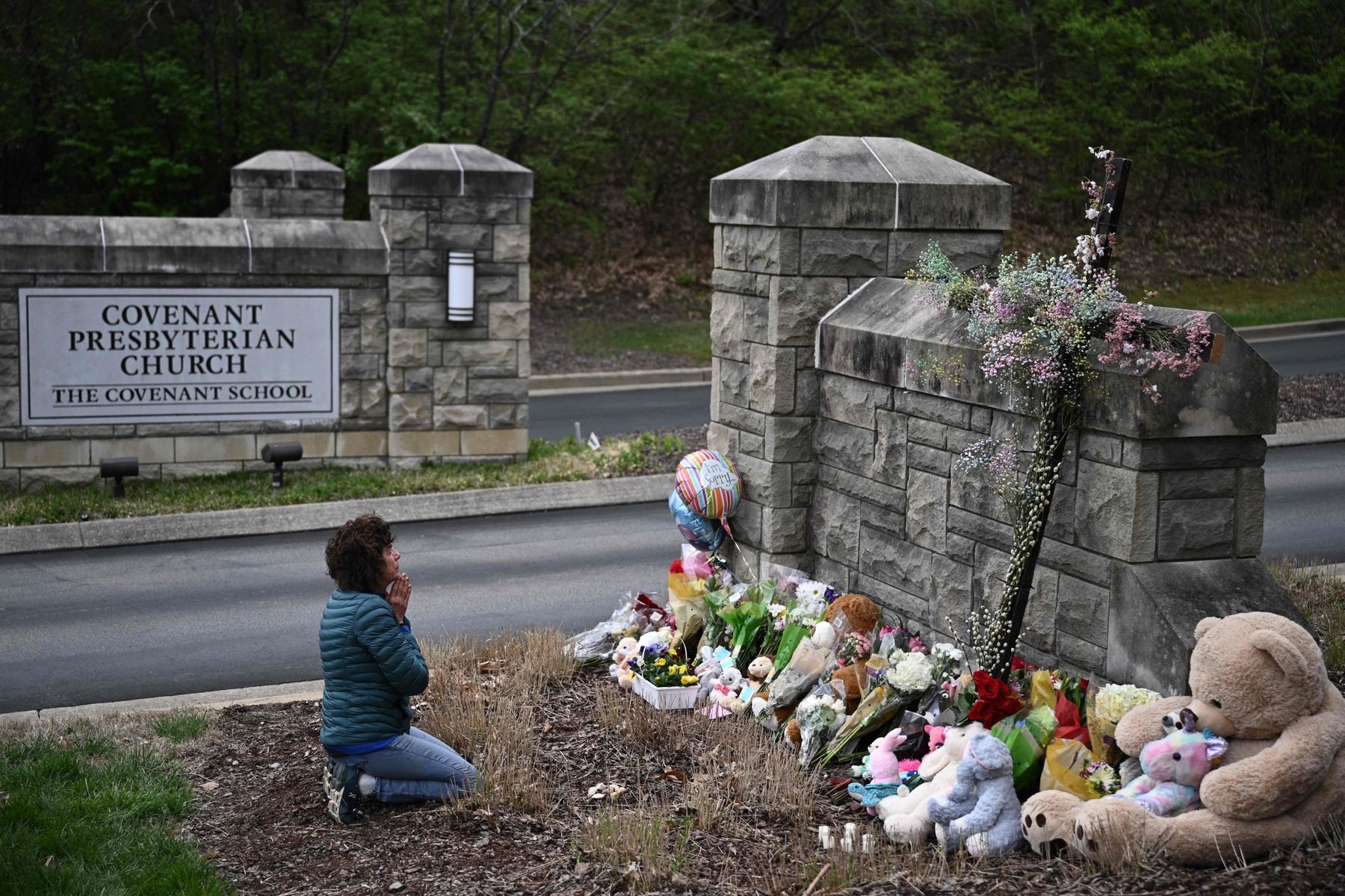 A person kneels at a memorial outside of the Covenant School.