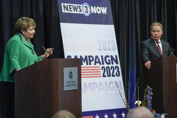 Janet Protasiewicz and Dan Kelly stand at lecterns with a sign between them that says Campaign 2023 at the only one-on-one debate