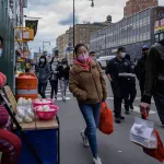 An asian woman wearing a facemask walks down the street in Flushing, Queens.