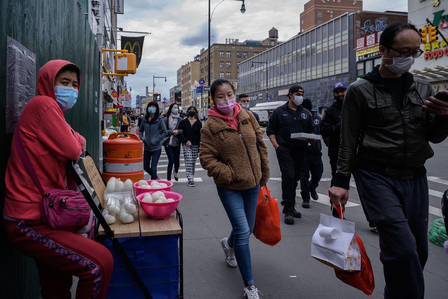 An asian woman wearing a facemask walks down the street in Flushing, Queens.