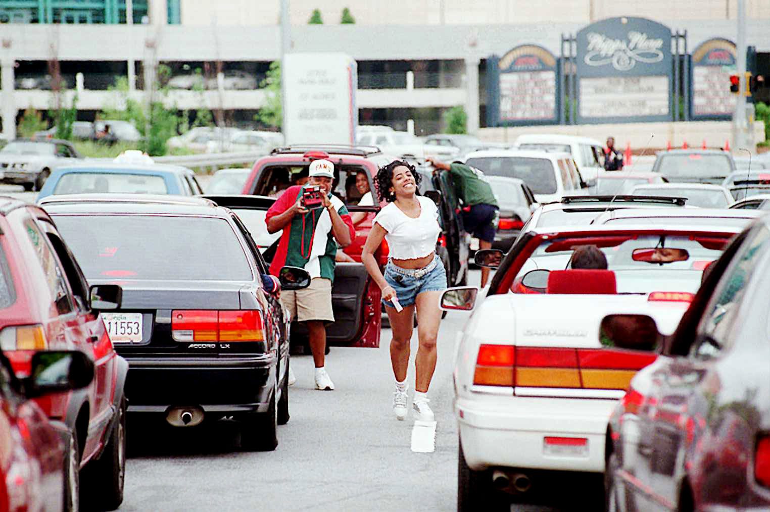 Woman running back to her car in the middle of traffic jam. She's carrying a Polaroid in her hand.