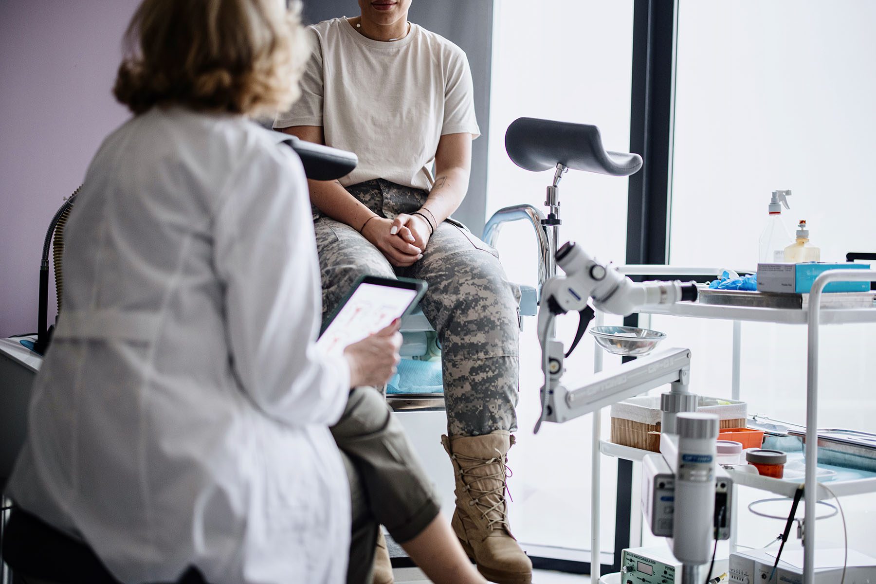 Patient in military uniform sitting on the exam table talking to her doctor.
