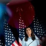 GOP Presidential candidate Nikki Haley stands in front of American flags at a podium giving a speech.
