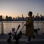 A mother with a stroller walks before the New York City skyline.