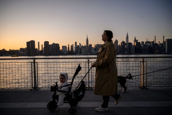 A mother with a stroller walks before the New York City skyline.