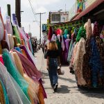A woman walks by rolls of fabric on a sunny afternoon outside of shops in the fashion district of Los Angeles.