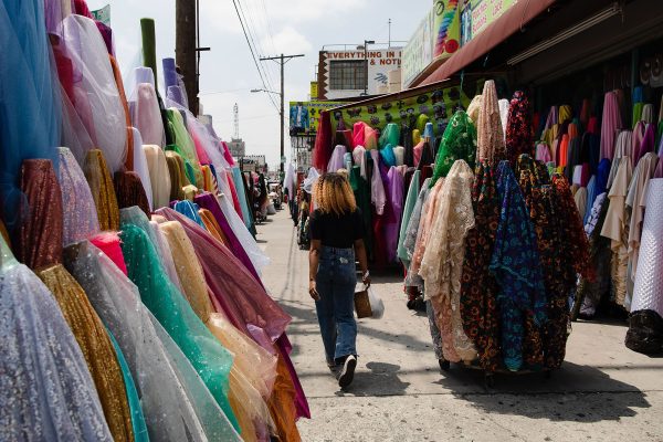 A woman walks by rolls of fabric on a sunny afternoon outside of shops in the fashion district of Los Angeles.