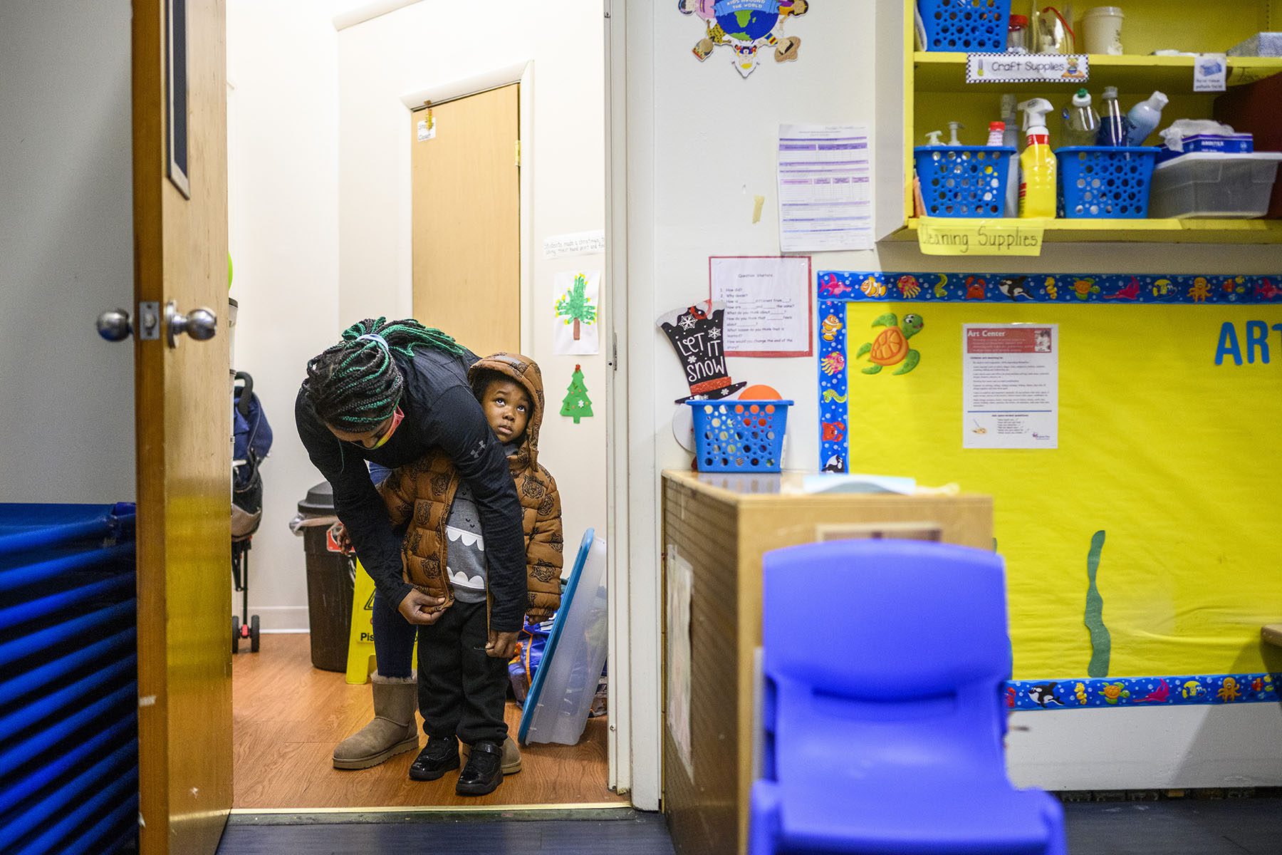 A teacher zips up a child's coat before recess.