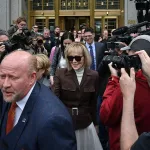 E. Jean Carroll departs the Manhattan Federal Court smiling while surrounded by lawyers and photojournalists.