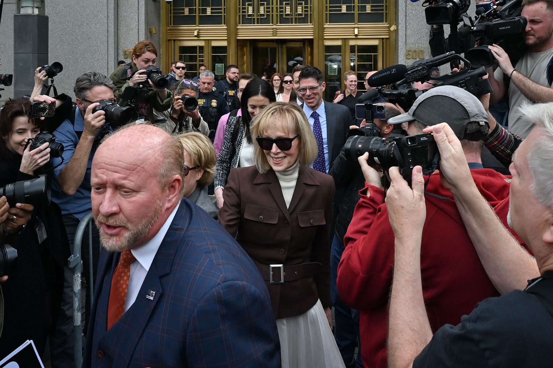 E. Jean Carroll departs the Manhattan Federal Court smiling while surrounded by lawyers and photojournalists.