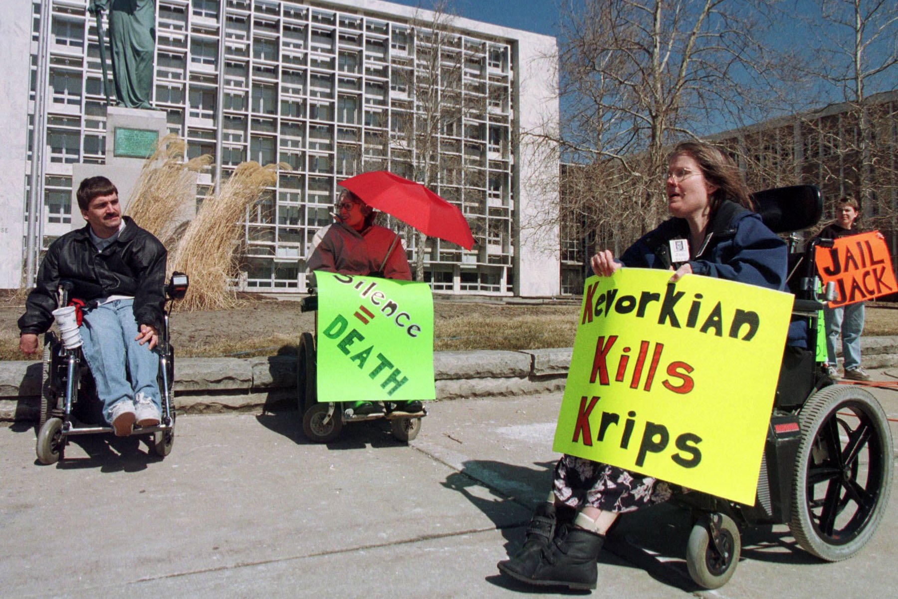 Diane Coleman and other demonstrators in wheelchairs protest outside of the Oakland County Courthouse. Coleman holds a sign that reads "Kevorkian Kills Krips."