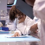 A young black woman in a lab coat is seen in a lab aboard OceanXplorer.