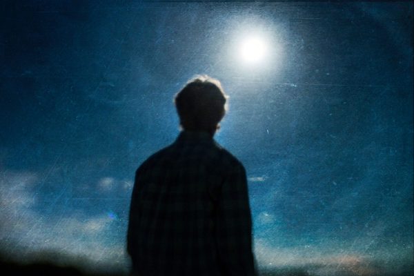 A man is silhouetted against the moon in this abstract photo.