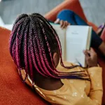 Young black girl reading a book on an orange chair.