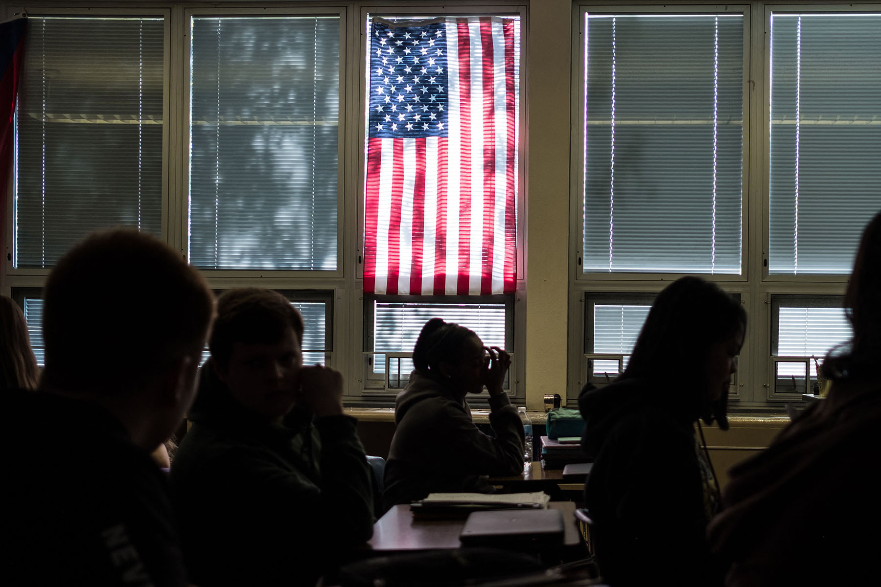 Students sit through class under a U.S. flag.