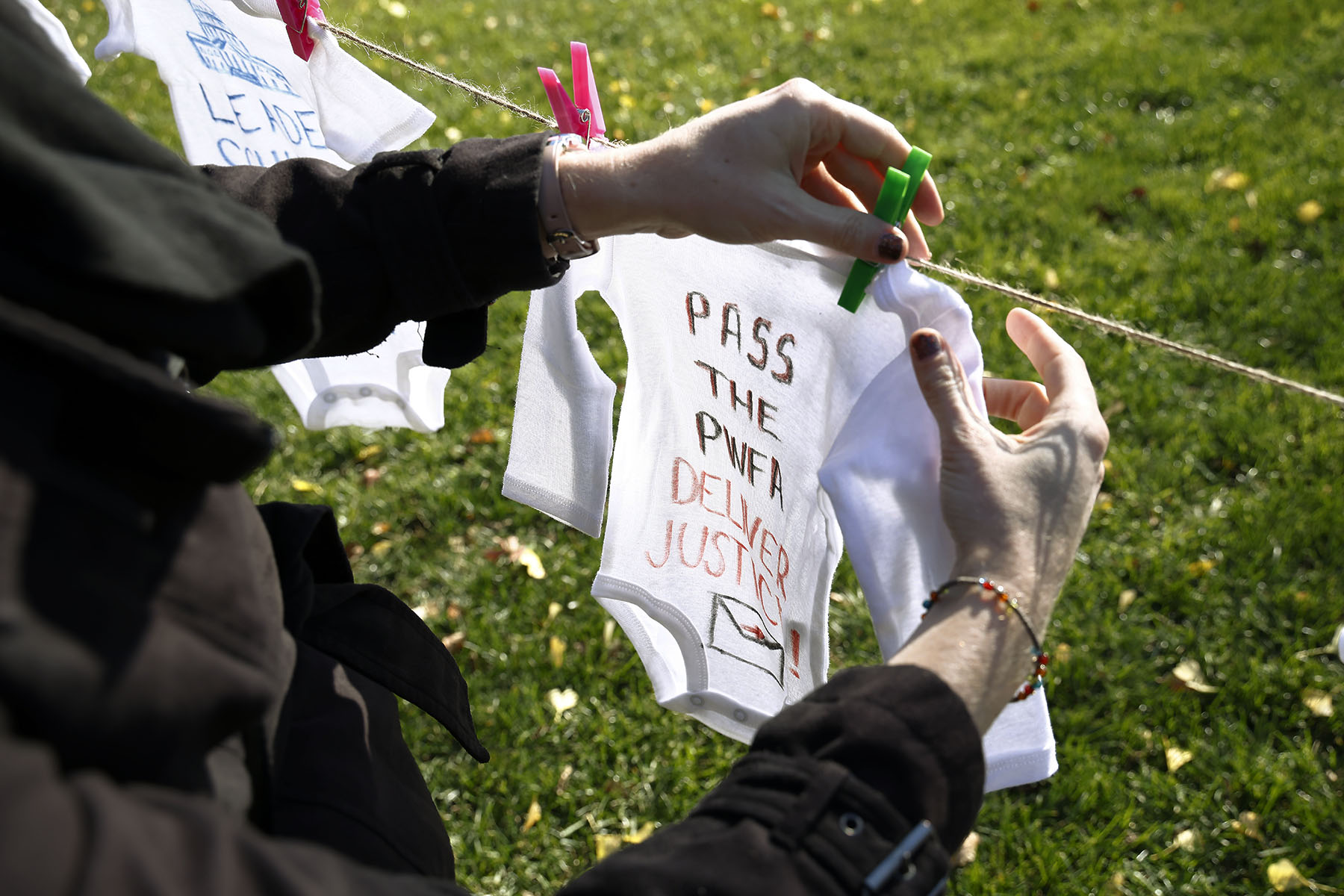 An activist pins a baby onesie with the words "pass the PWFA - Deliver Justice" written on it to a clothing line during a rally.