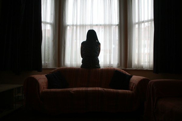 A silhouetted woman looks out a window in a dark room.