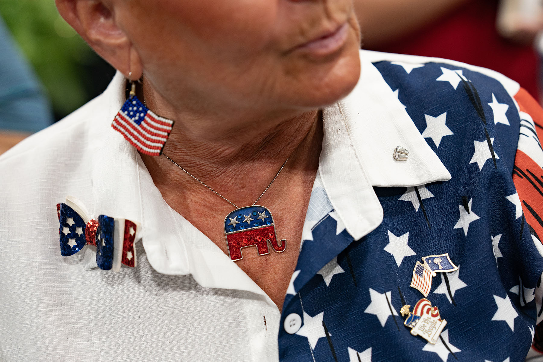 A woman wears a an American flag shirt, American flag earrings and a Republican elephant necklace as Nikki Haley speaks during a campaign event.