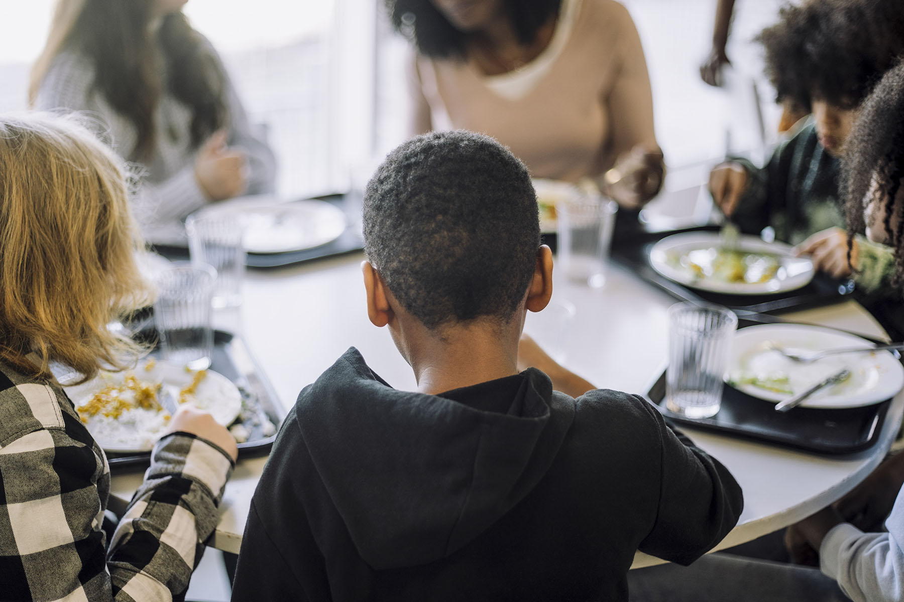 Rear view of boy sitting with friends at table in cafeteria during lunch