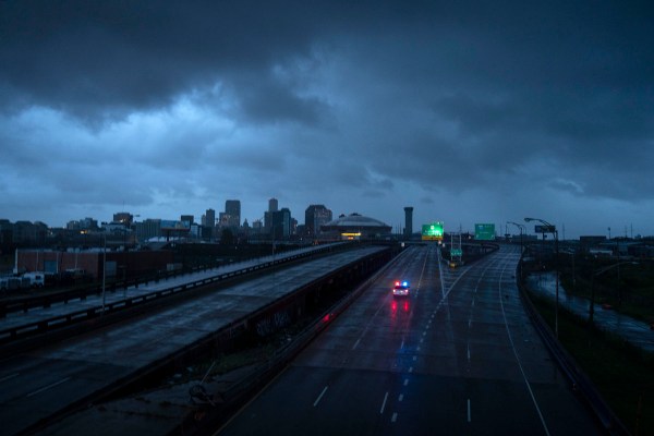 A police car drives through an empty highway as the New Orleans skyline is seen shrouded in dark clouds in the horizon.