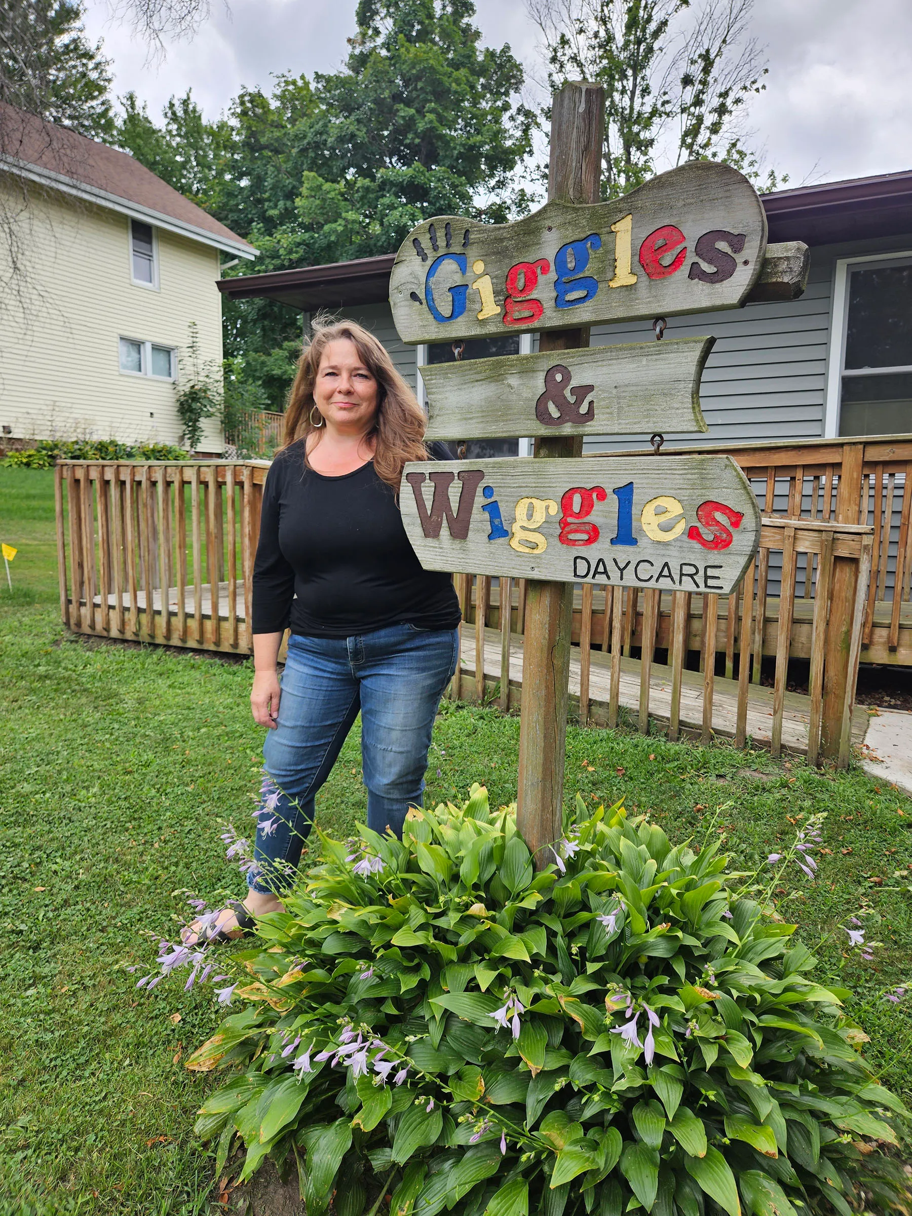 Kristin Holman-Steffel poses next to the "giggles and wiggles daycare" sign.