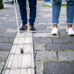 image of visually impaired people holding a cane walking down the street.