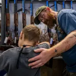 A father helps his son steady a firearm during the National Rifle Association's annual convention in May 2022 in Houston, Texas.