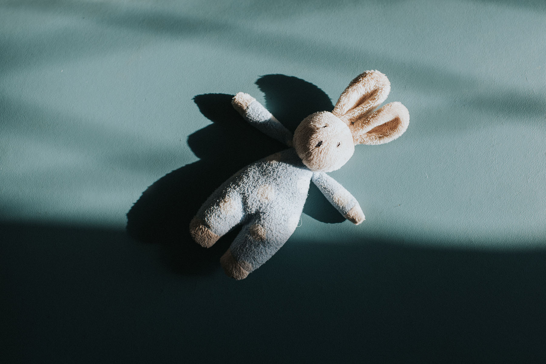 Moody image of a small soft blue toy bunny.
