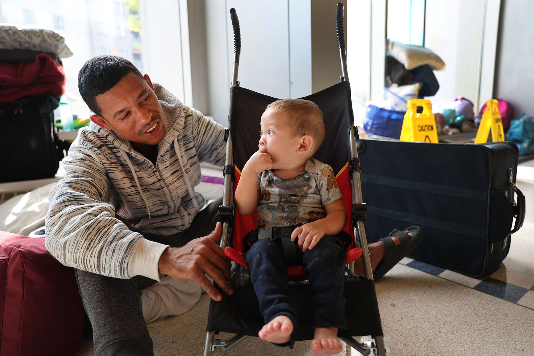 A migrant father from Venezuela entertains his 15-month-old son in the lobby of a Chicago police station.