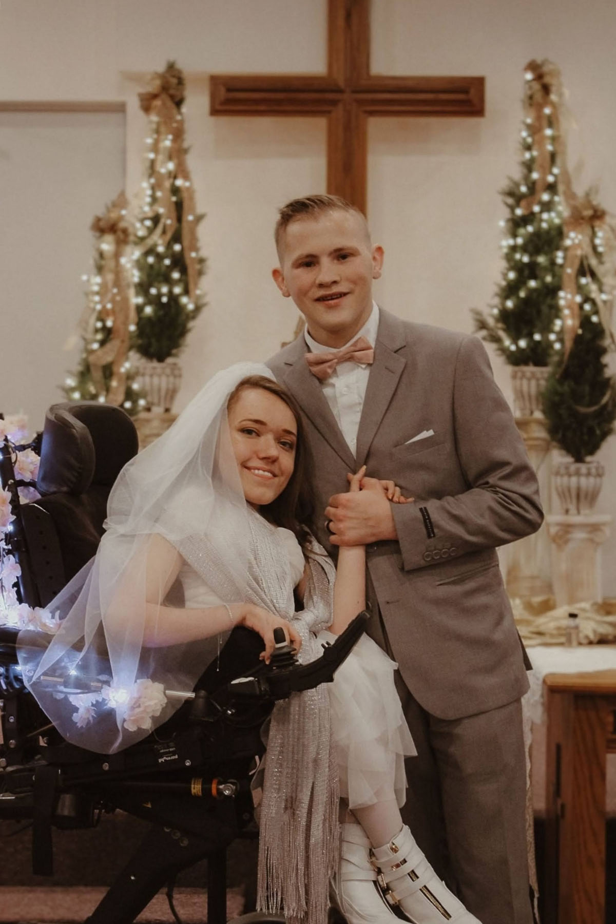Amber Weise, wearing her wedding dress, and her husband hold hands in church during their wedding day.