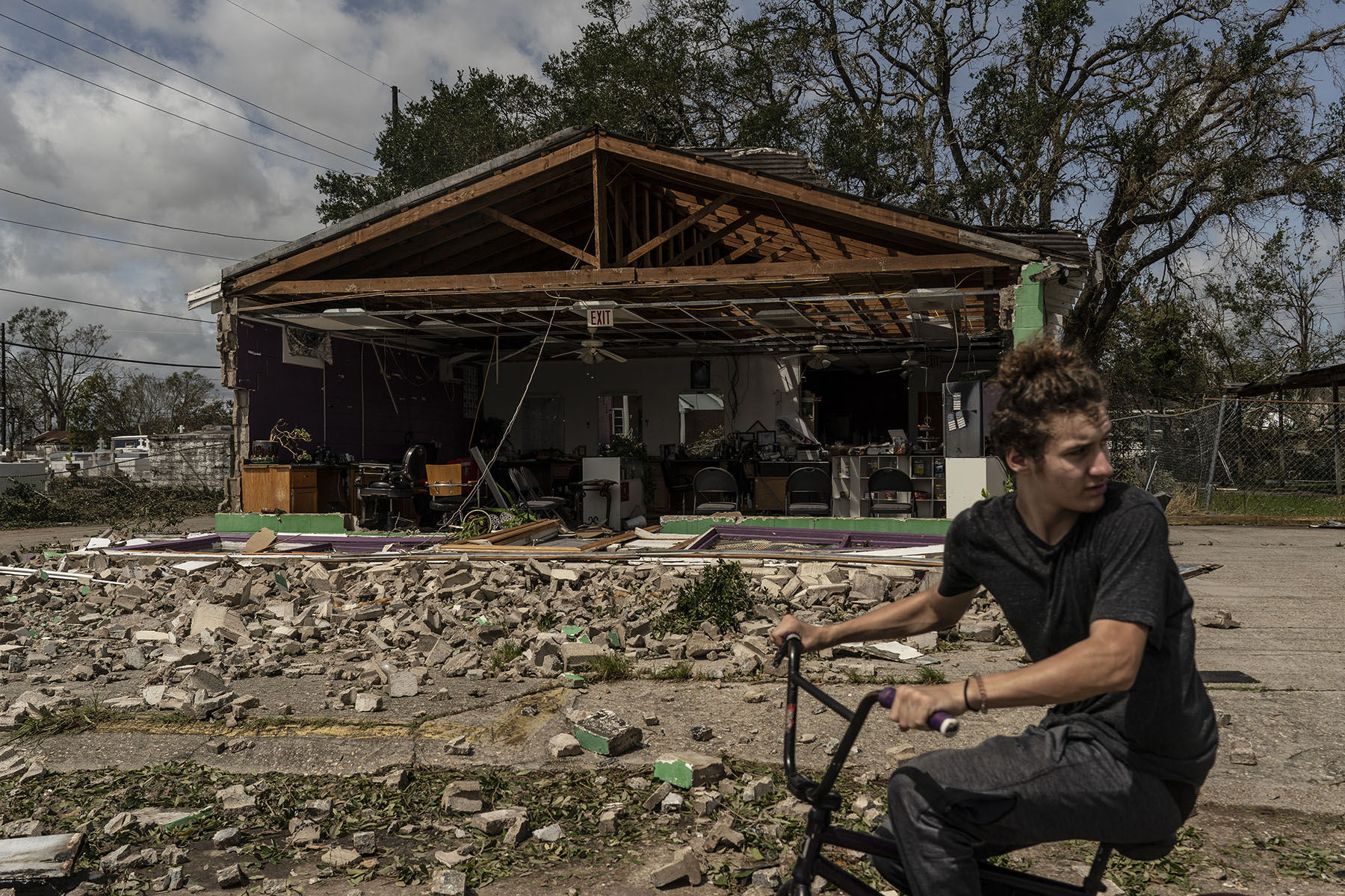 A man rides a bicycle in front of a damaged property.