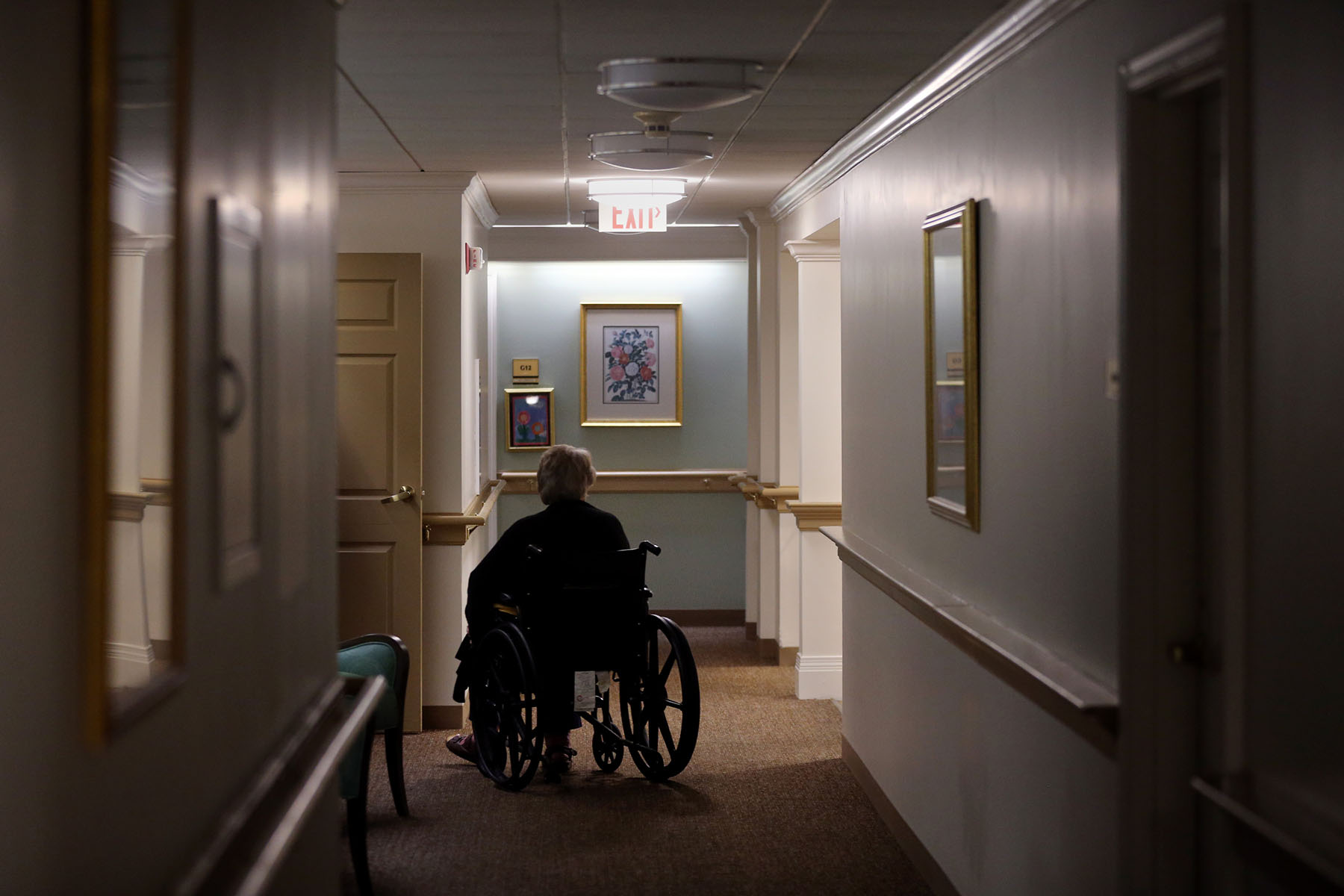 A resident is seen sitting in a wheelchair at the end of a hallways in an assisted living facility.