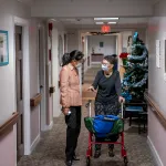 Tina Sandri, CEO of Forest Hills of DC senior living facility, left, helps a resident on walker back to her room.