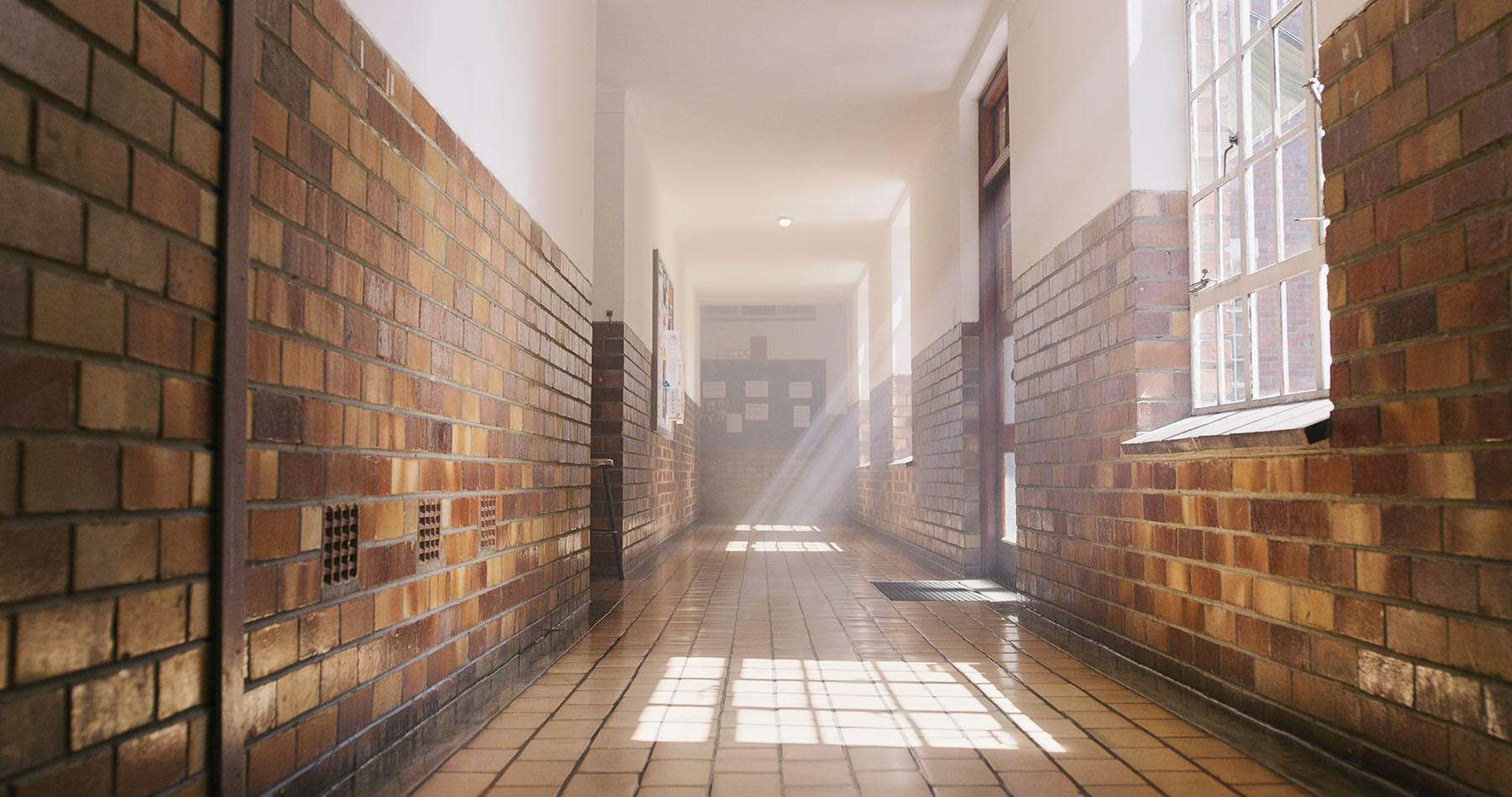 Light filters into a hallway through a window in an empty school.