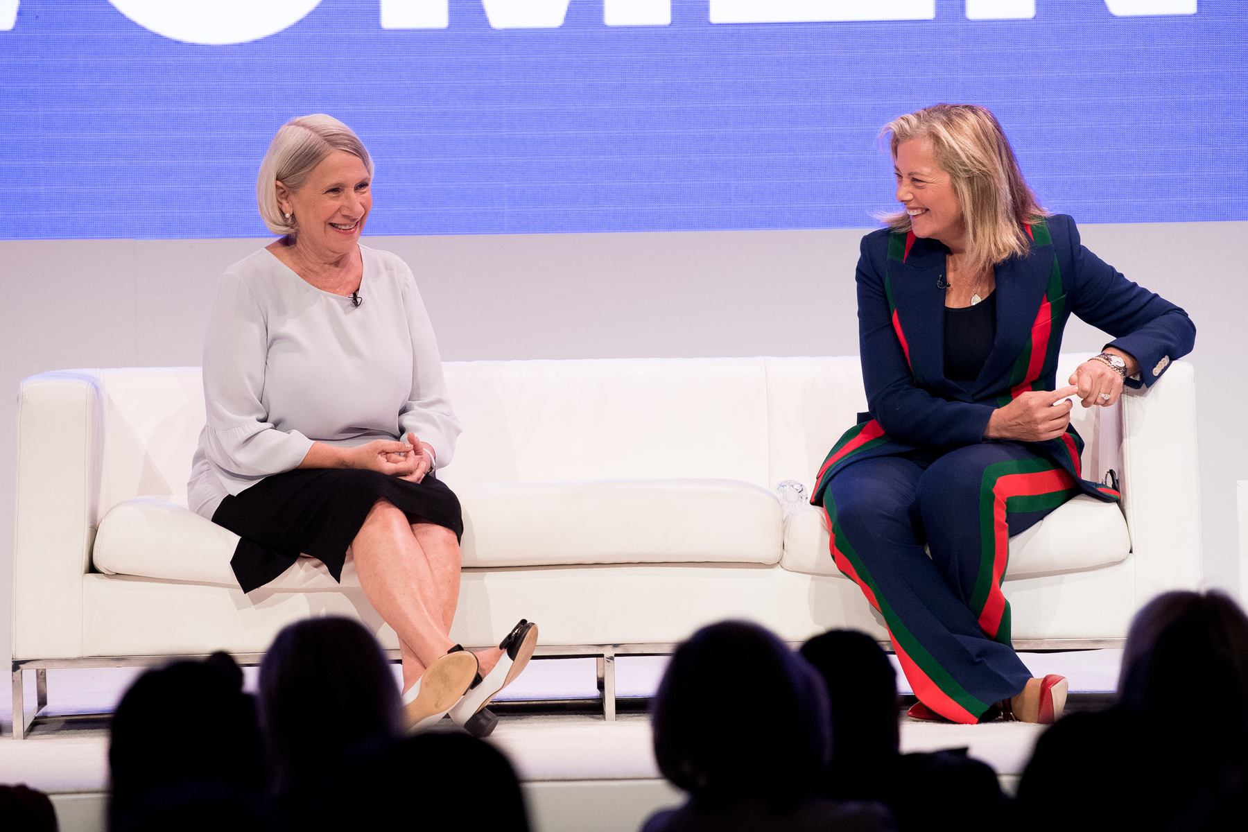 Two women speak on a white stage.