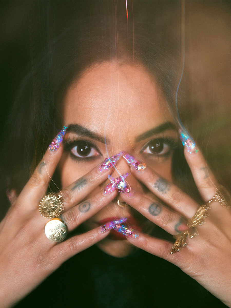 A close-up image of Bri Luna's eyes and tattooed hands dressed in gold jewelry.