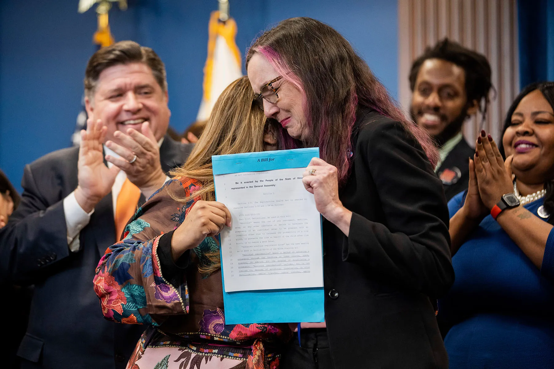 State Rep. Kelly Cassidy and state Sen. Celina Villanueva hug each other as they hold the signed House Bill 4664.