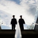 the silhouette of two college graduates in cap and gown climbing up a set of steps.