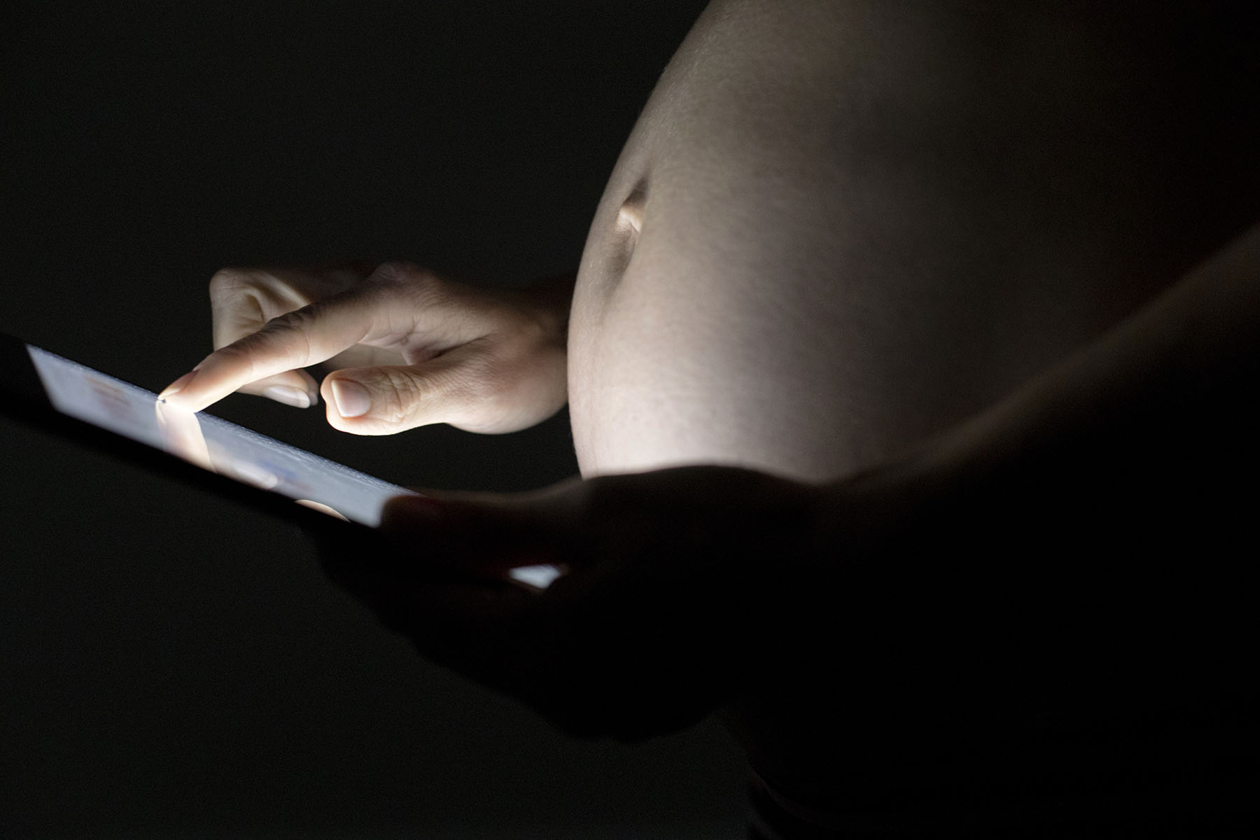 Pregnant woman using a digital tablet in dark.