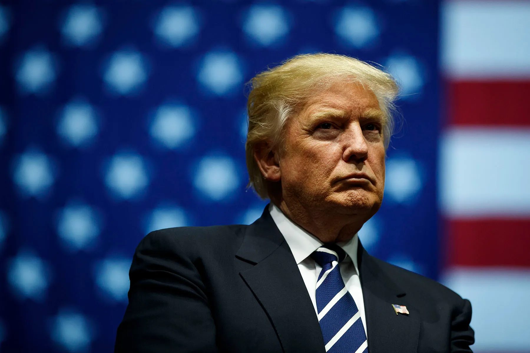 Donald Trump looks on during a rally, behind him is an American flag.