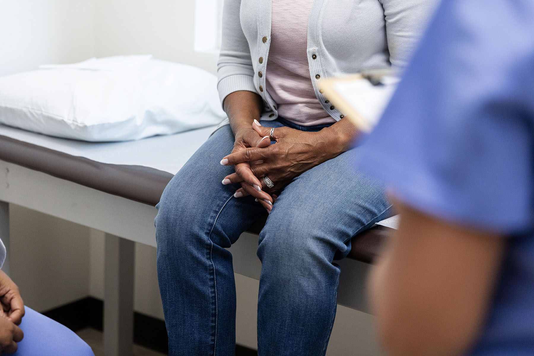 Low angle view as an unrecognizable senior adult woman clasps her hands during a discussion with two unrecognizable medical personnel.