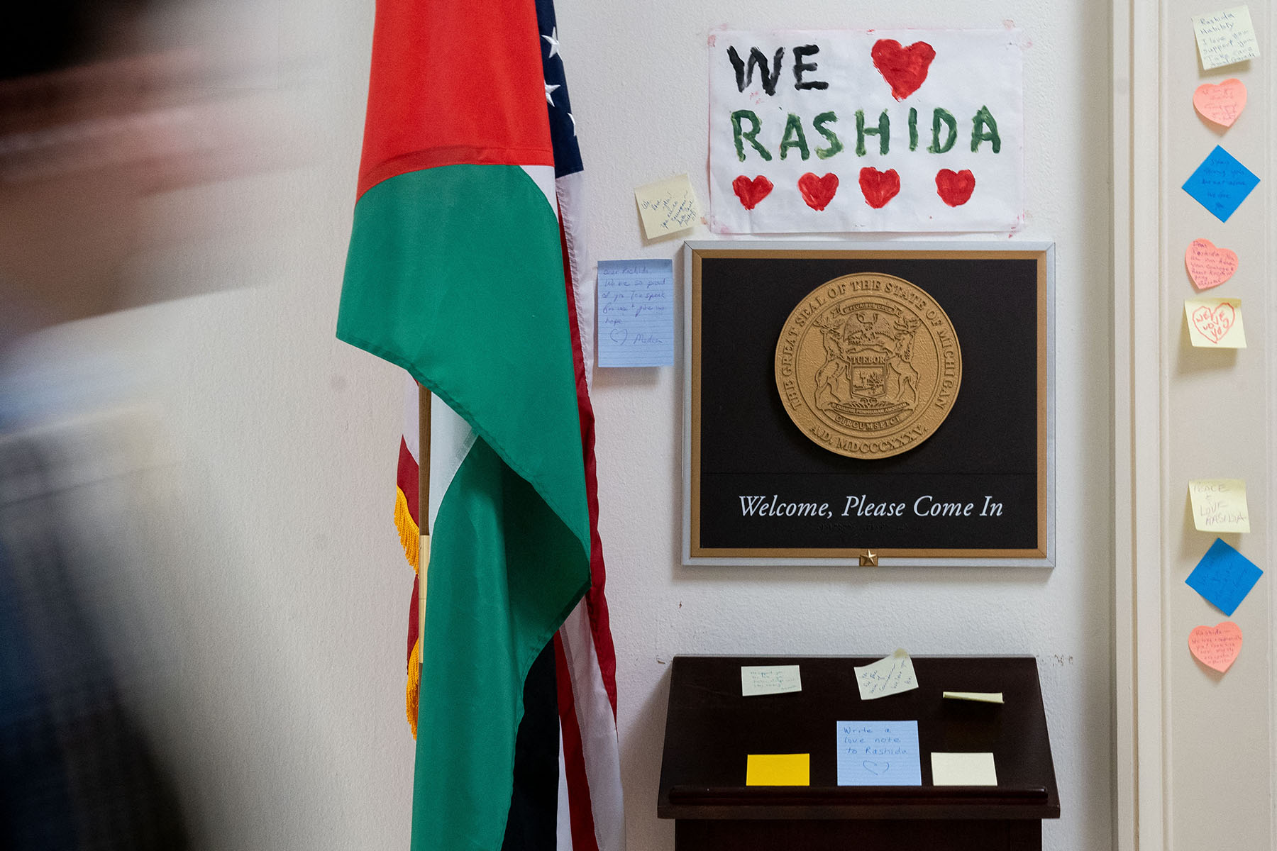 A person walks past signs and notes left outside the office of Rep. Rashida Tlaib. One reads "We heart RASHIDA."