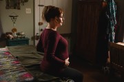 Sara Toups sits on a bed and holds her pregnant belly at her home.