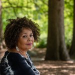 A Black woman with curly hair sits in a forest.