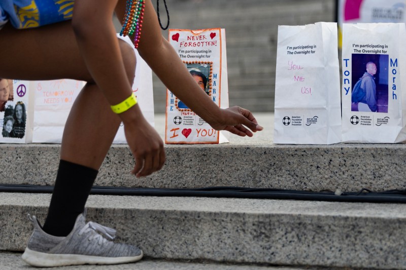 A participant reaches for a luminary bag displaying the photo of a loved one, during the American Foundation for Suicide Prevention Overnight Walk near the Lincoln Memorial in Washington, D.C., on Saturday, June 3, 2023.