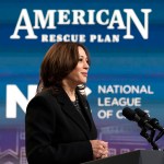 Vice President Kamala Harris speaks at a podium on the White House campus while American Rescue Plan signage is seen behind her.