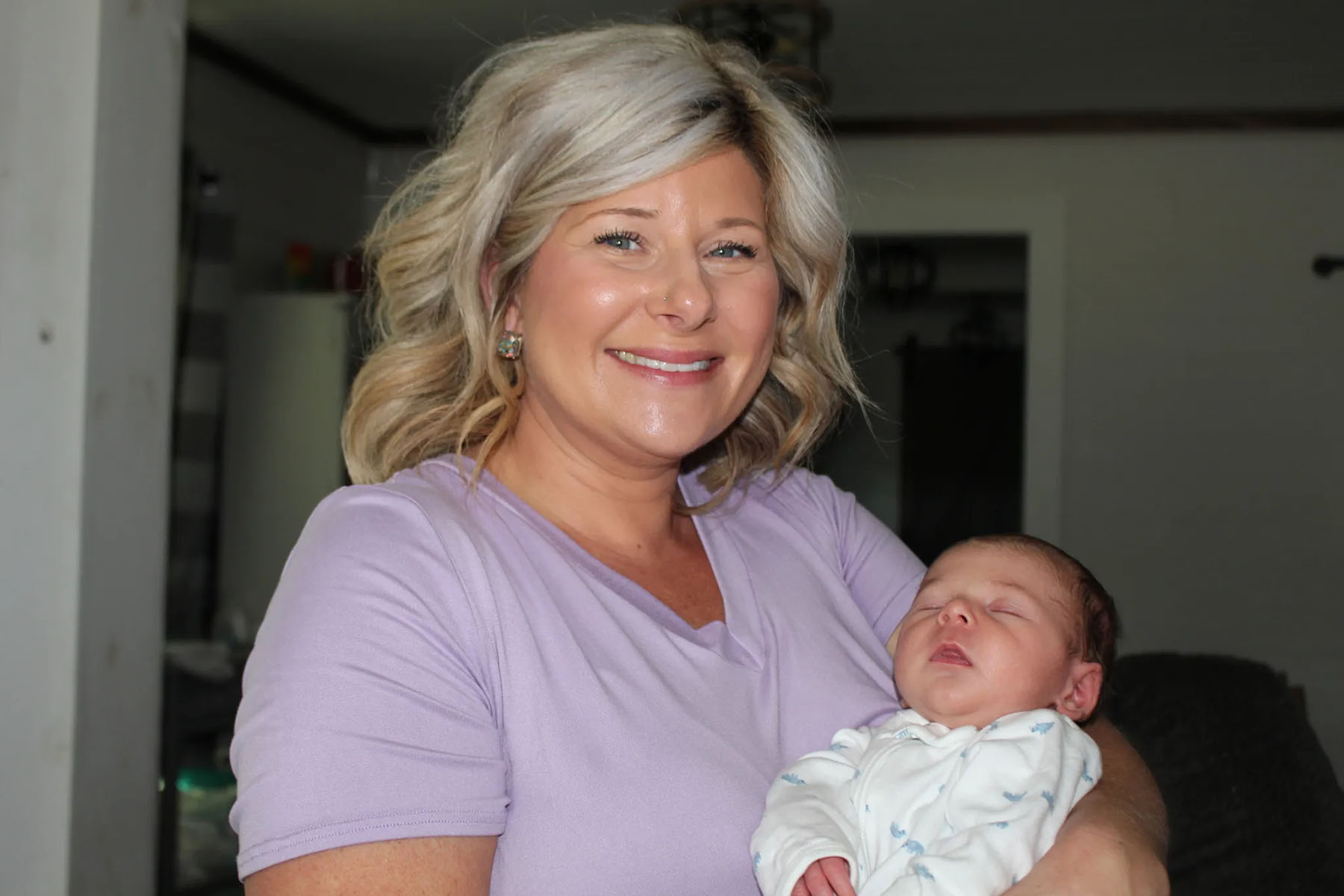 Deanna Buckins holds her sleeping infant and smiles.