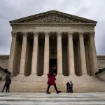 People walk in front of the U.S. Supreme Court on a cloudy day.