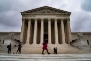 People walk in front of the U.S. Supreme Court on a cloudy day.