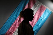 Silhouette of a man standing in front of a transgender pride flag.